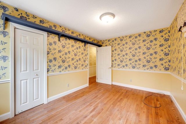 spare room with wallpapered walls, light wood-style floors, baseboards, and wainscoting