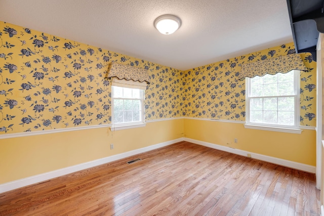 unfurnished room with visible vents, a textured ceiling, light wood-style floors, wallpapered walls, and baseboards