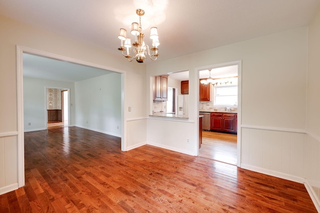 unfurnished dining area featuring a chandelier, wainscoting, and wood finished floors