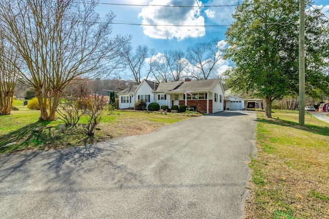 single story home with aphalt driveway, a chimney, a garage, brick siding, and a front lawn