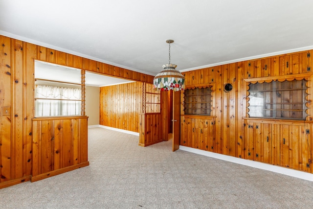 unfurnished room featuring carpet floors, a chandelier, wood walls, baseboards, and ornamental molding