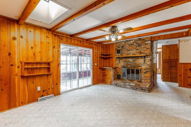 unfurnished living room with visible vents, wood walls, carpet, a fireplace, and beam ceiling