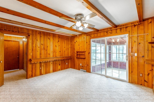 carpeted spare room with beamed ceiling, visible vents, wooden walls, and ceiling fan