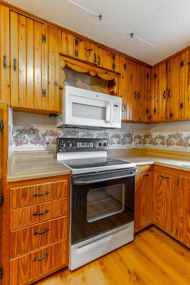 kitchen featuring light countertops, light wood finished floors, range with electric stovetop, white microwave, and brown cabinets