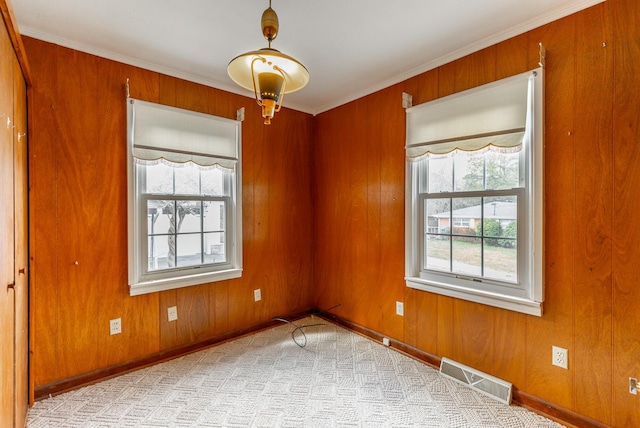 unfurnished room with crown molding, wood walls, carpet, baseboards, and visible vents