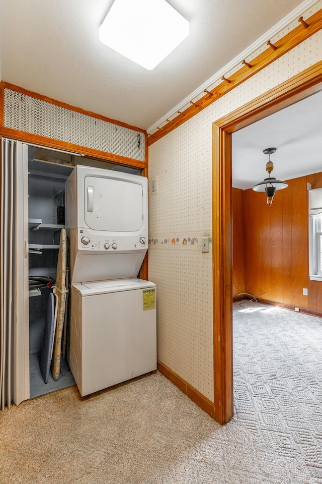 laundry area featuring carpet floors, stacked washing maching and dryer, baseboards, wallpapered walls, and ornamental molding