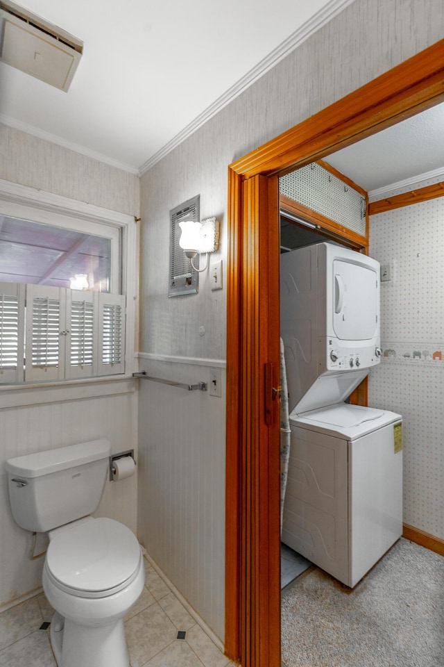 bathroom featuring stacked washer and dryer, tile patterned floors, toilet, wallpapered walls, and ornamental molding