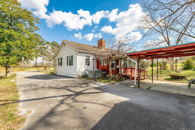 view of front of home with driveway, a chimney, a wooden deck, and a carport