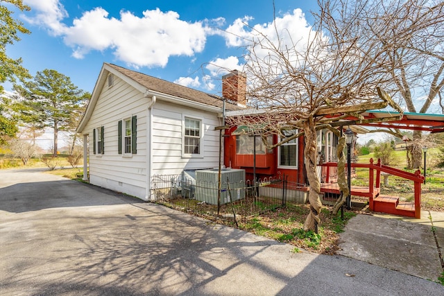view of front facade featuring cooling unit, crawl space, a fenced front yard, aphalt driveway, and a chimney