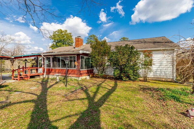rear view of house with a lawn, a sunroom, a shingled roof, and a chimney