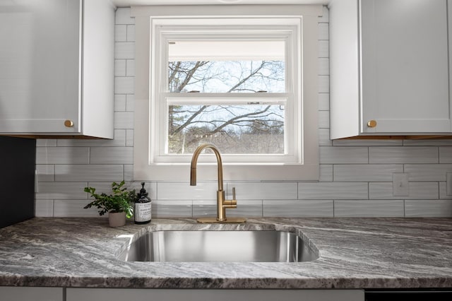 details with a sink, decorative backsplash, light stone counters, and white cabinets