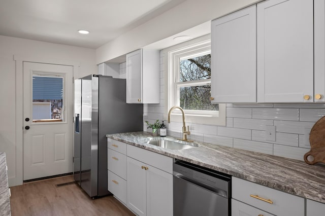 kitchen with a sink, tasteful backsplash, white cabinetry, appliances with stainless steel finishes, and light stone countertops