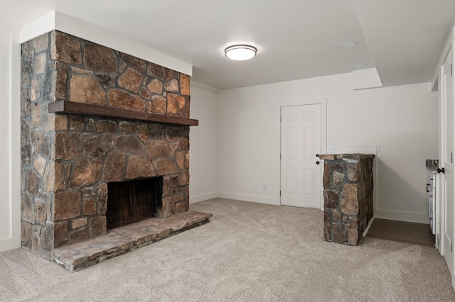 unfurnished living room with a stone fireplace, baseboards, and carpet floors