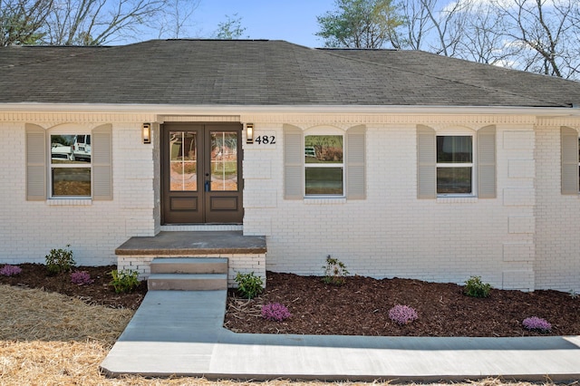 doorway to property featuring french doors, brick siding, and a shingled roof