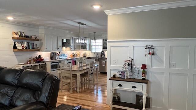 interior space with a wainscoted wall, ornamental molding, appliances with stainless steel finishes, wood finished floors, and wall chimney exhaust hood