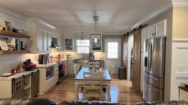 kitchen with a sink, crown molding, appliances with stainless steel finishes, a barn door, and wall chimney range hood