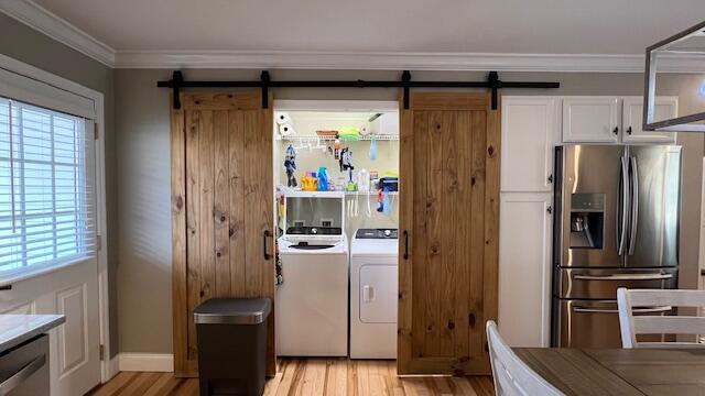 laundry area with light wood finished floors, a barn door, ornamental molding, laundry area, and independent washer and dryer