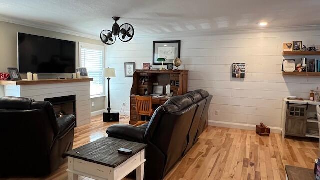 living area featuring crown molding, baseboards, a chandelier, a fireplace, and light wood-style floors