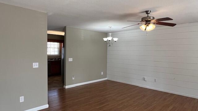 unfurnished room with ceiling fan with notable chandelier, dark wood-type flooring, and baseboards