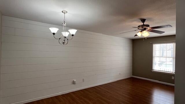 spare room featuring ceiling fan with notable chandelier, dark wood-type flooring, and baseboards