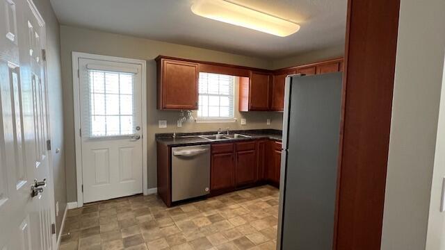 kitchen featuring baseboards, a sink, appliances with stainless steel finishes, dark countertops, and brown cabinets