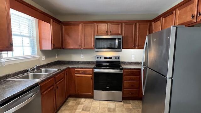 kitchen with a sink, dark countertops, brown cabinetry, and stainless steel appliances