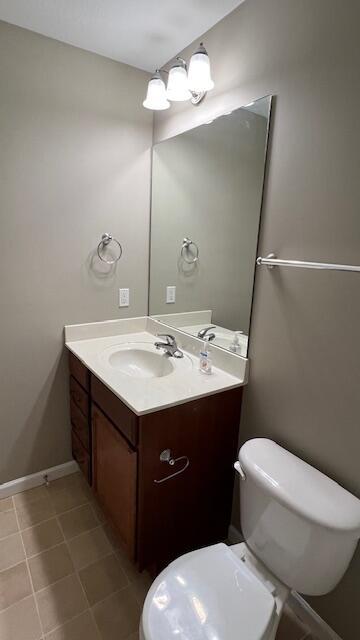 half bathroom with baseboards, toilet, vanity, and tile patterned flooring