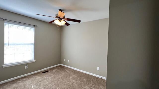 carpeted spare room featuring visible vents, baseboards, and a ceiling fan