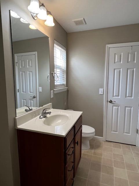 bathroom featuring visible vents, toilet, vanity, and baseboards