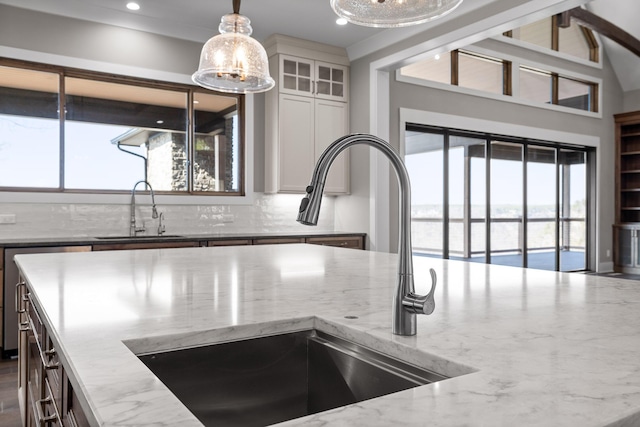 interior details with hanging light fixtures, backsplash, light stone countertops, and a sink