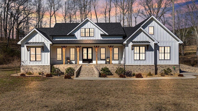 modern farmhouse featuring a porch, a yard, board and batten siding, and brick siding