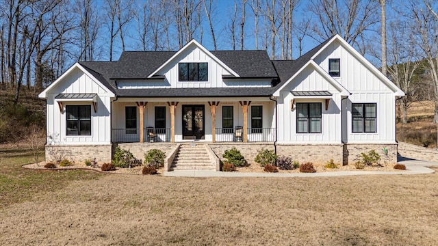 modern farmhouse style home with a front yard, roof with shingles, a porch, board and batten siding, and brick siding