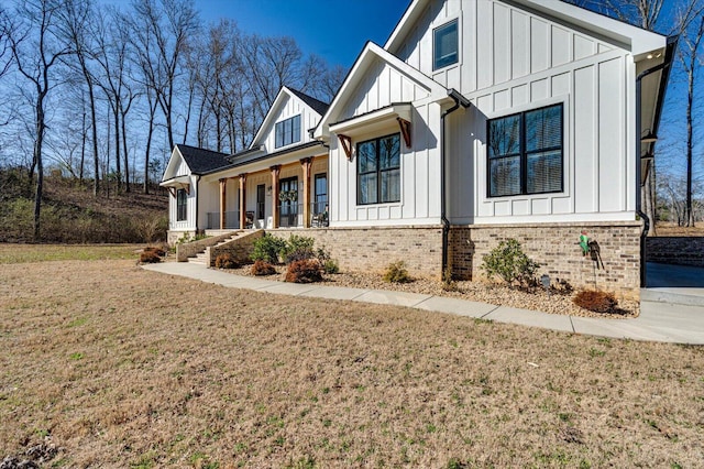 view of front of house with brick siding, covered porch, board and batten siding, and a front lawn