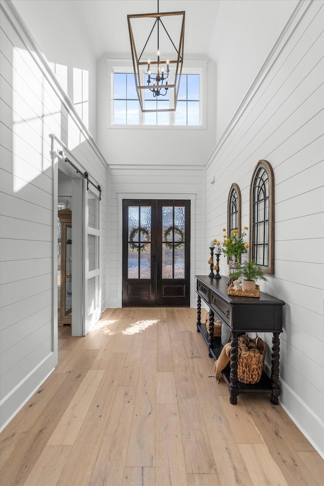 entryway featuring a barn door, french doors, a high ceiling, a notable chandelier, and wood-type flooring