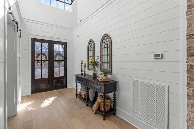 entrance foyer with visible vents, light wood-style flooring, a towering ceiling, and french doors