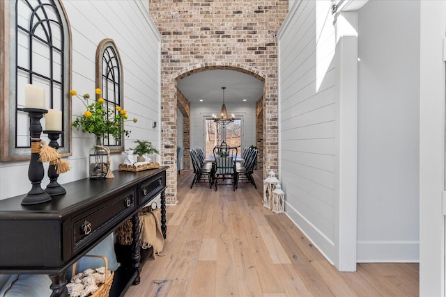 hallway featuring arched walkways, a notable chandelier, light wood-style flooring, and brick wall