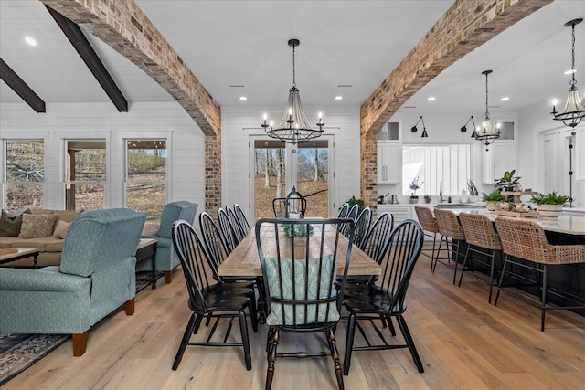 dining room featuring light wood finished floors, beamed ceiling, and an inviting chandelier