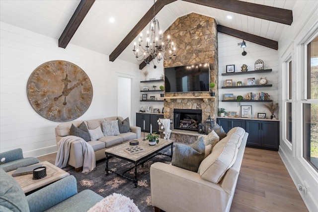 living room with beam ceiling, a stone fireplace, an inviting chandelier, and wood finished floors