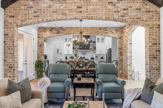 living area with arched walkways, an inviting chandelier, brick wall, and light wood finished floors