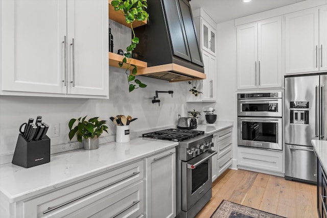 kitchen with premium range hood, appliances with stainless steel finishes, white cabinets, and light wood finished floors