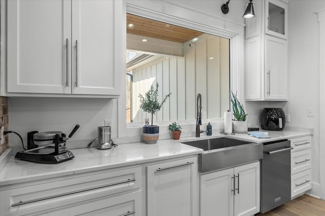 kitchen featuring light stone counters, dishwasher, white cabinetry, and a sink