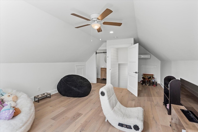 sitting room with light wood finished floors, baseboards, a wall mounted air conditioner, lofted ceiling, and a ceiling fan