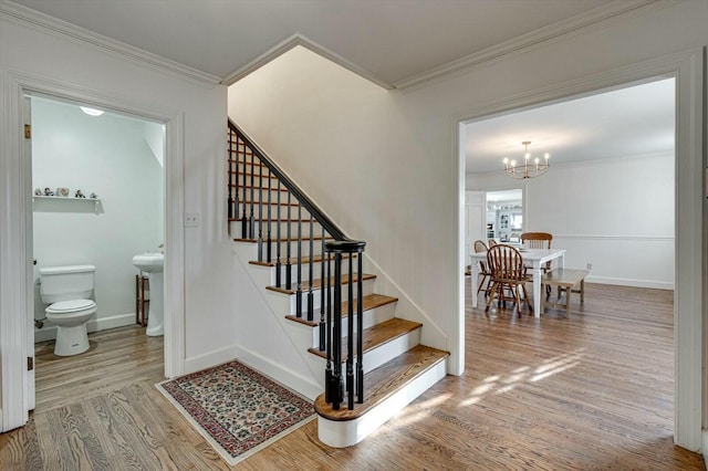 stairway featuring a chandelier, crown molding, baseboards, and wood finished floors