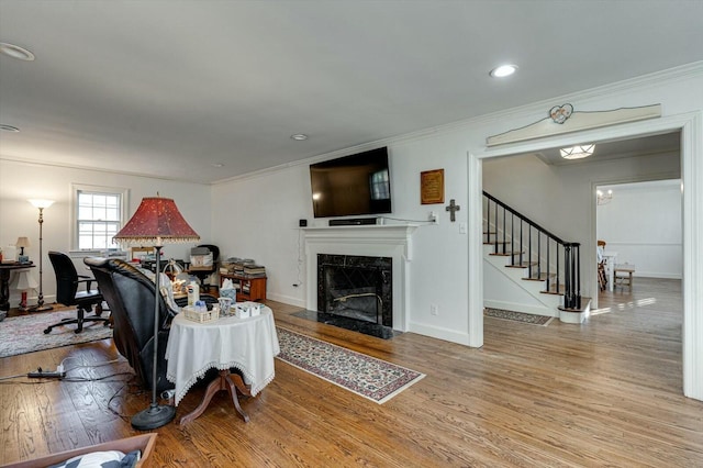 living room with a high end fireplace, crown molding, stairs, and wood finished floors