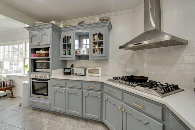 kitchen with gray cabinets, crown molding, stainless steel appliances, and wall chimney exhaust hood