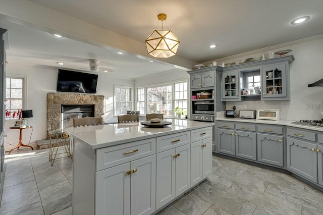 kitchen featuring gray cabinetry, a stone fireplace, light countertops, crown molding, and backsplash