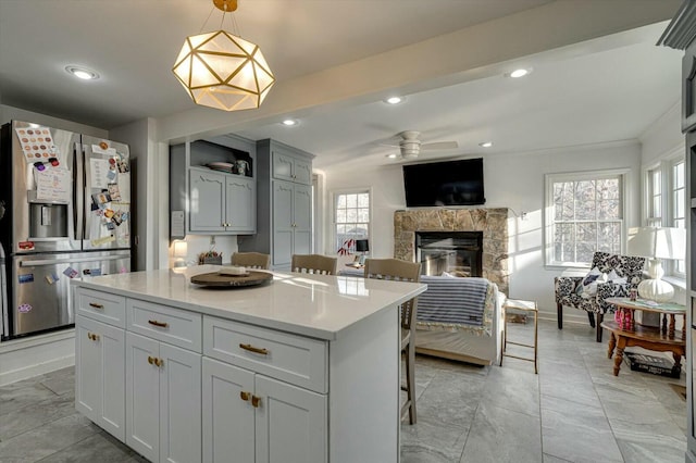 kitchen with a center island, light countertops, recessed lighting, a fireplace, and stainless steel refrigerator with ice dispenser