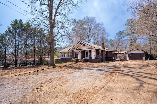 view of front of home with driveway, a chimney, and fence