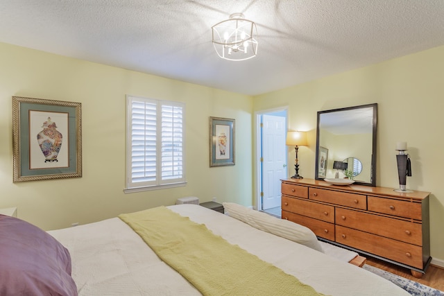 bedroom with an inviting chandelier, wood finished floors, and a textured ceiling