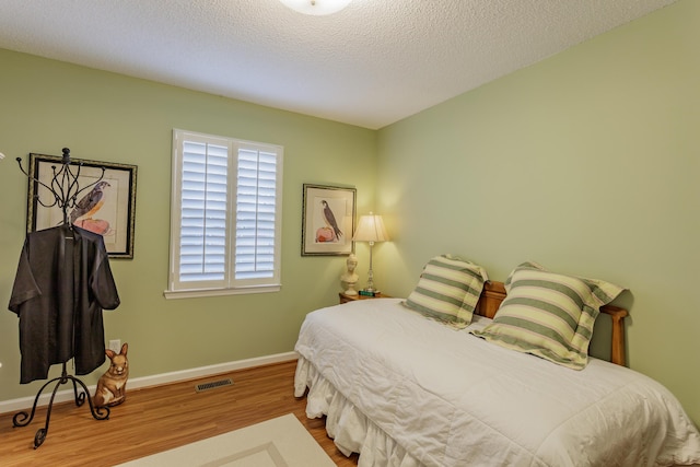 bedroom with visible vents, a textured ceiling, baseboards, and wood finished floors